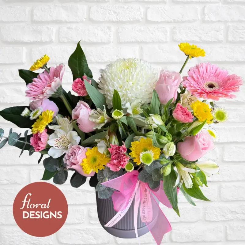 Arreglo floral Siena con rosas rosadas, gerberas, crisantemos y alstroemerias en base decorativa con listón rosa