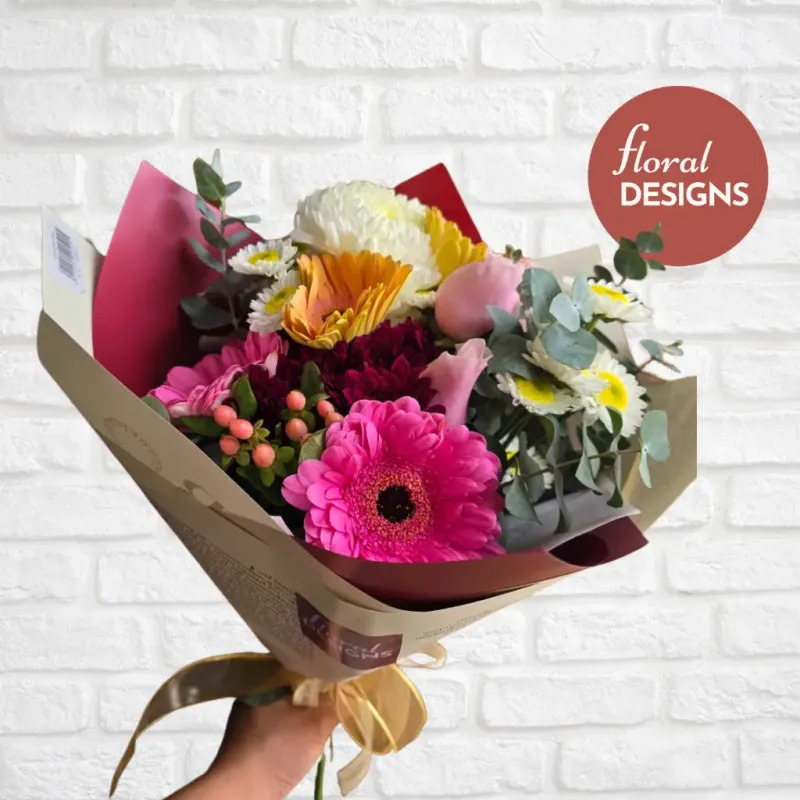 Bouquet de flores naturales con gerberas rosadas, rosas, crisantemos, margaritas y eucalipto en empaque decorativo.