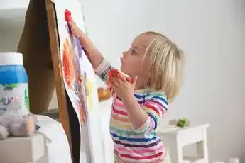 MUCKI Finger Paint white 150 ml jar with colorful children’s artwork in the background.
