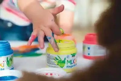 Child using MUCKI finger paints with hands on paper