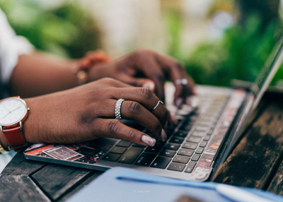 Close-up of a pair of black women&#39;s hands typing on a keyboard in a cozy home office, with warm lighting and a creative, inviting atmosphere.
