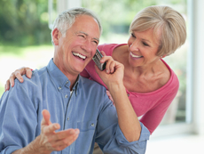Man talking on cordless amplified telephone while his wife looks on