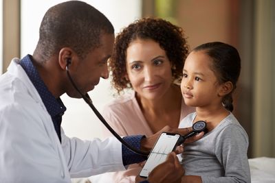 A doctor uses a Littmann digital stethoscope to listen to a child&#39;s breathing, while the child&#39;s mother holds her.