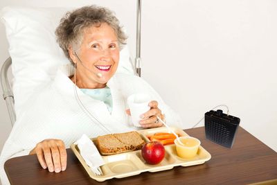 An elderly woman in a hospital bed using an ALDS MiniBuddy for voice amplification.
