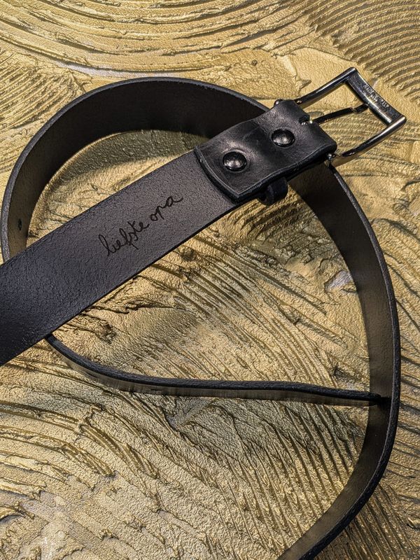 Close-up van gepersonaliseerde inscriptie op zwarte leren herenriem van Atelier Loulou