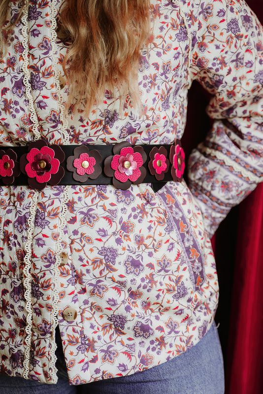 Close-up van leren bloemen op zwarte tailleriem Full Bloom van Atelier Loulou over gebloemde blouse