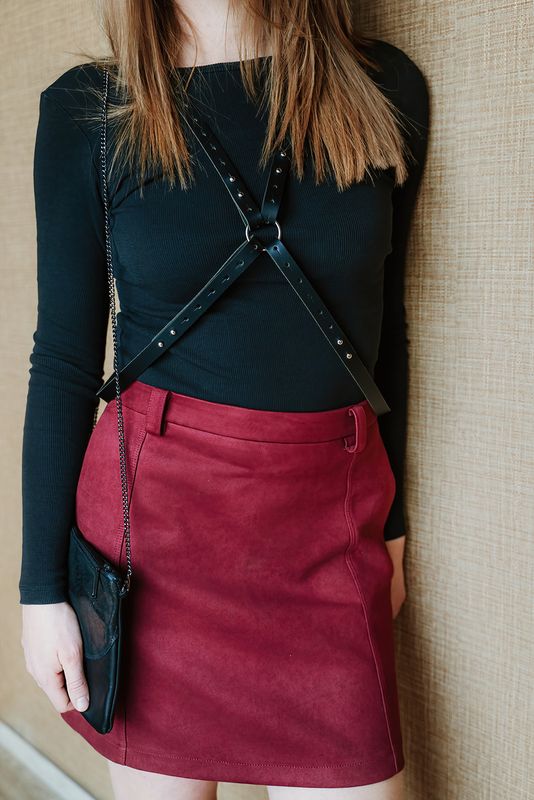 Vrouw draagt handgemaakt leren tuigje Cross My Heart van Atelier Loulou over zwarte top en rode rok