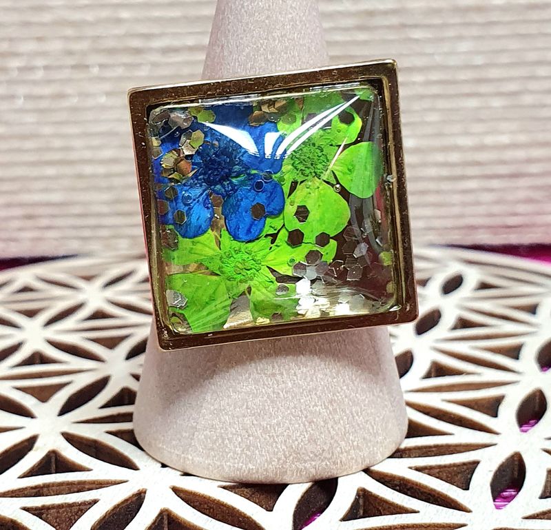 💐 Bague ouverte en acier doré inoxydable. Cabochon carré en verre bombé. Petites fleurs séchées bleues et vertes. Création artisanale. Modèle unique.