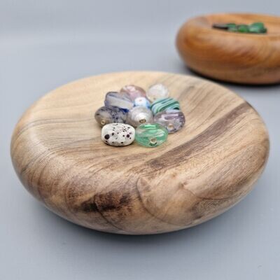 Poplar trinket dish with striking grain pattern, doughnut shape with dimple on surface in which sits some glass beads. 