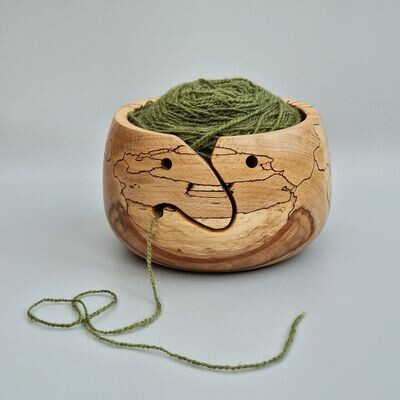 Large wooden yarn bowl hand turned from a highly figured piece of spalted beech, with unusual inclusion shaped like a smile. The shape of the apertures have been designed to portray a smiling face. The bowl is holding a 100g ball of wool. Perfect for knitters and crocheters.
