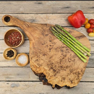 Handcrafted oak burr chopping/serving board with sculpted handle and natural edge, shown on a rustic surface.