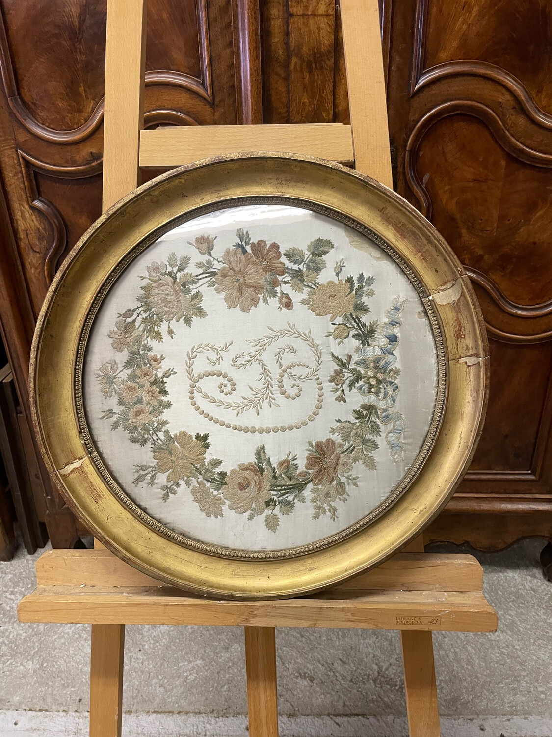 Soie brodée d'un monogramme et d'une guirlande de fleurs; Dans un cadre rond en bois doré. Début XIX°. Diam 53 cm