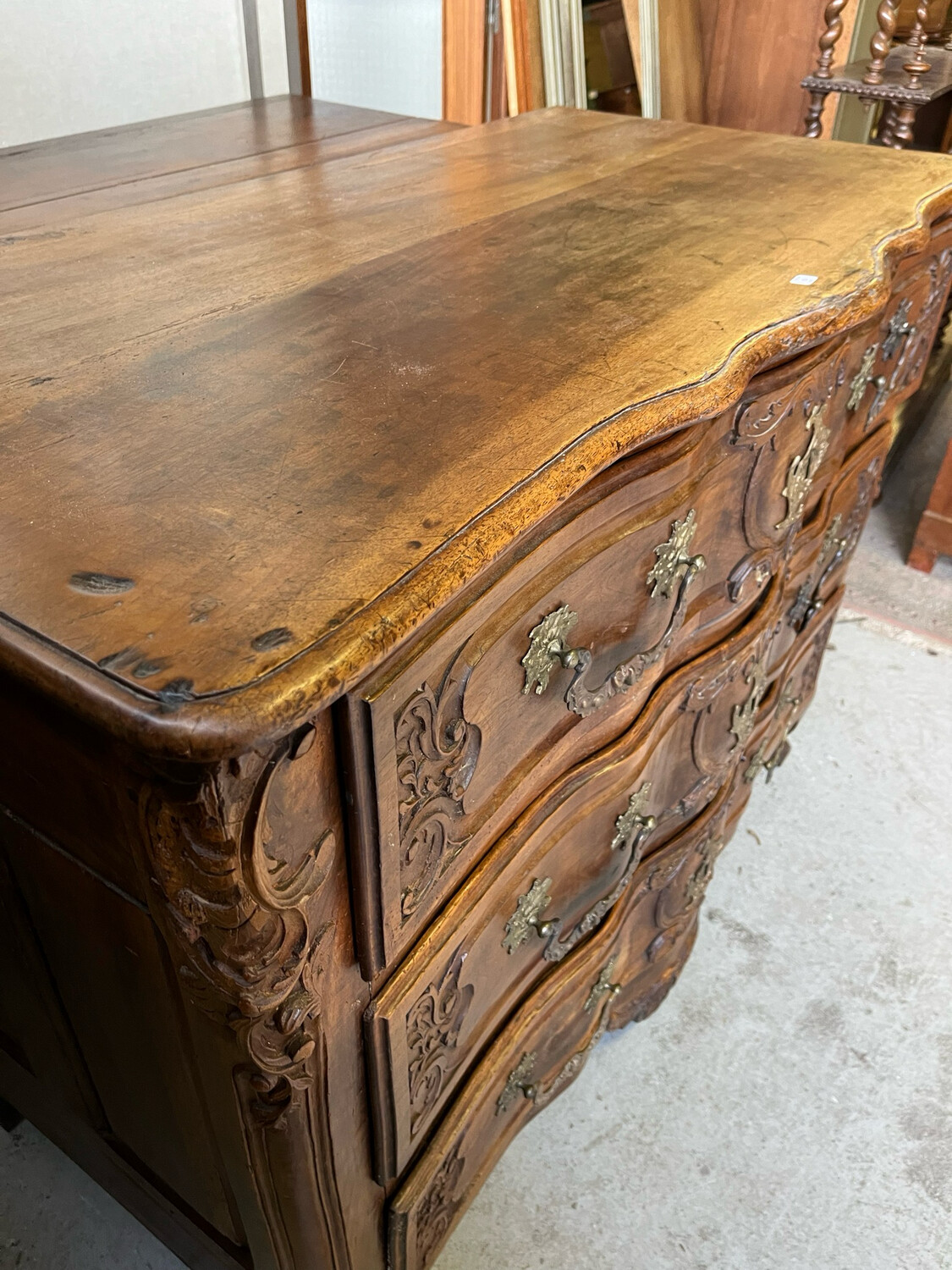 Commode en noyer richement mouluré et sculpté, ouvrant par trois tiroirs. Ornementation de bronze doré. XVIII ème siècle. H 103,5 x L 135 x P 70 cm.