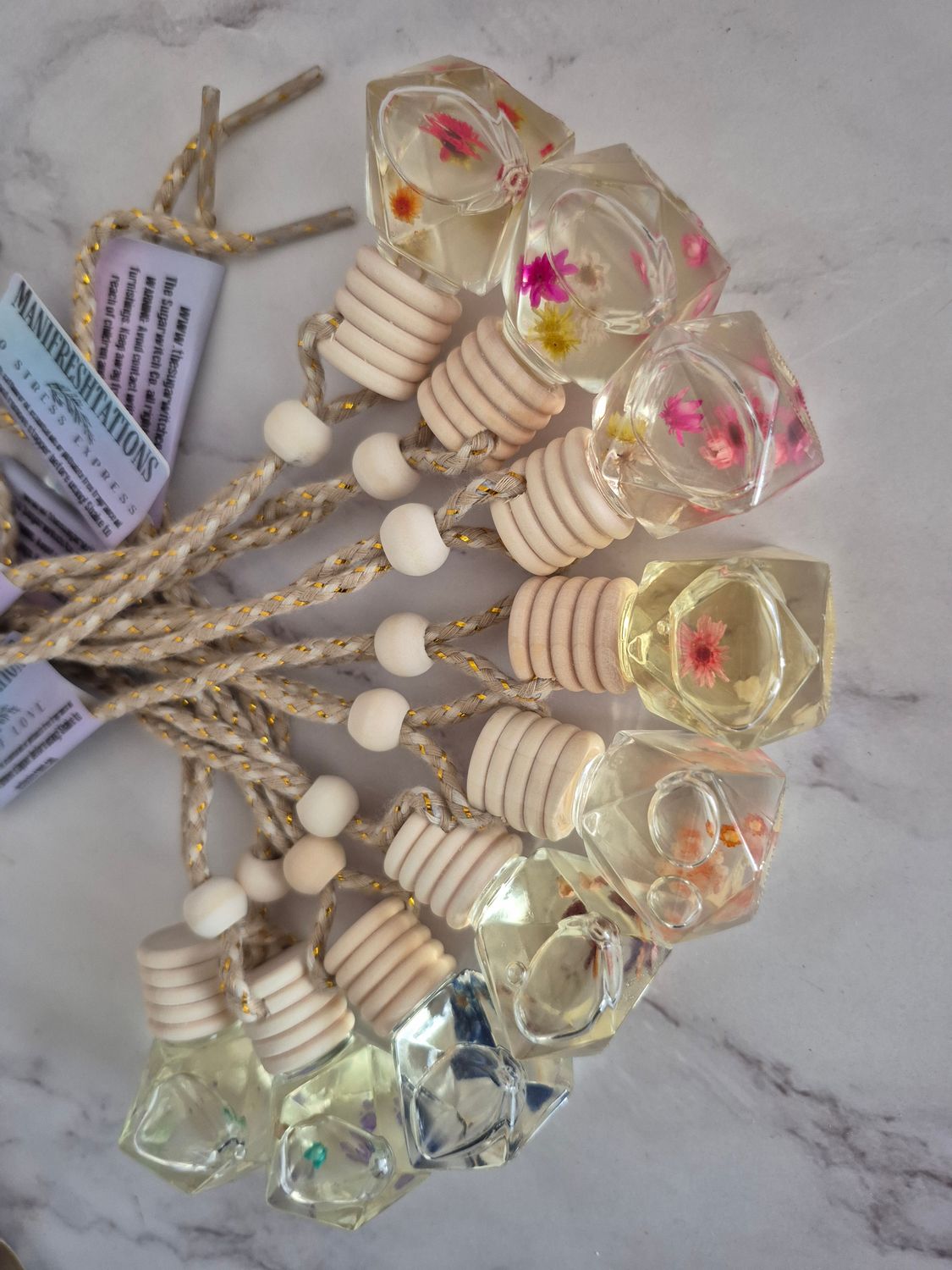 Flower filled car diffuser with gemstone shaped glass bottle, reed diffuser cap, and adjustable rope