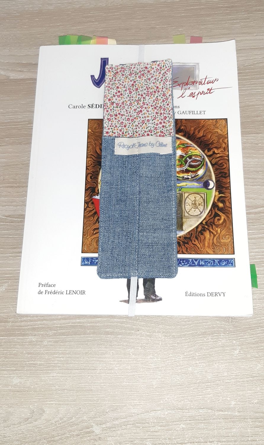 Marque-page Jorma cousu main en jean recyclé et tissu fleuri, posé sur un livre grand format