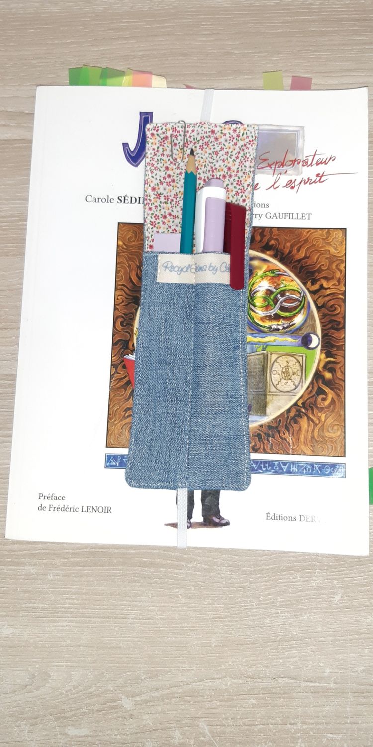 Marque-page Jorma cousu main en jean recyclé et tissu fleuri, posé sur un livre grand format