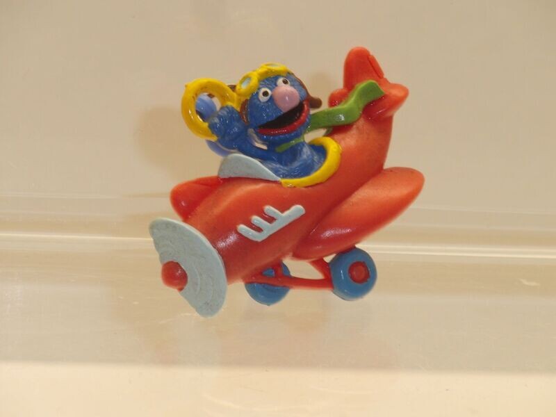 Sesamstraße: ca. 90er Jahre: Grobi im Flugzeug (Flachfigur als Anhänger) Sesamstraße: ca. 90er Jahre: Grobi im Flugzeug (Flachfigur als Anhänger)