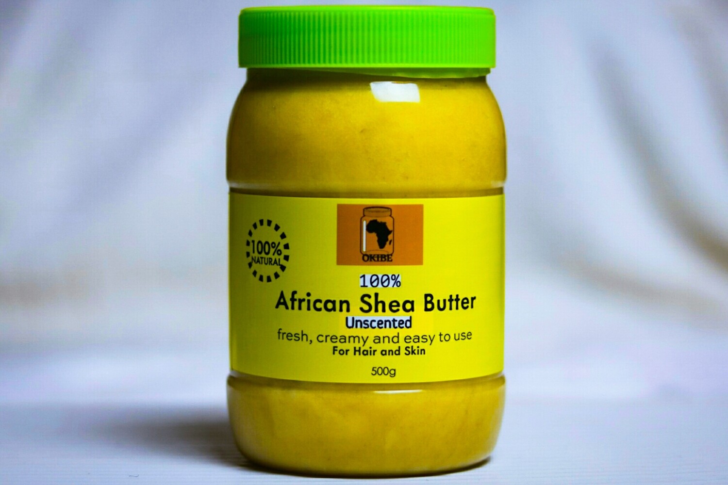 A jar of Okibe Unrefined 100% African shea butter placed on a table with white background.