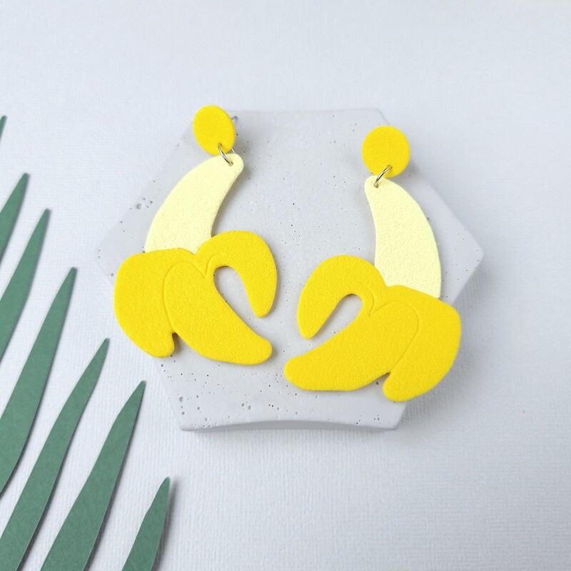 A pair of large yellow and cream banana-shaped earrings, made from polymer clay, that have a textured, modern design.
