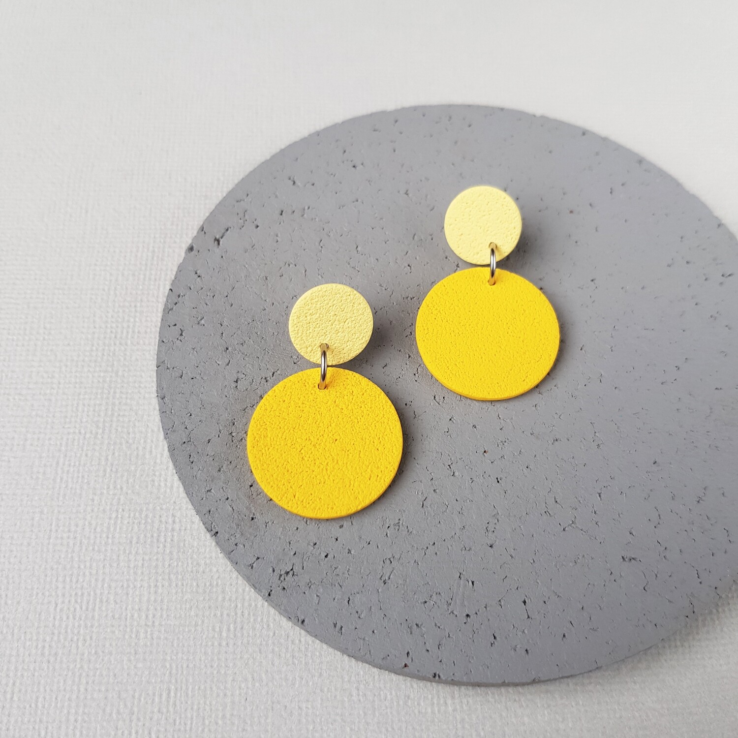 A pair of yellow and cream coloured circle earrings. The earrings are made of polymer clay and have a textured surface.