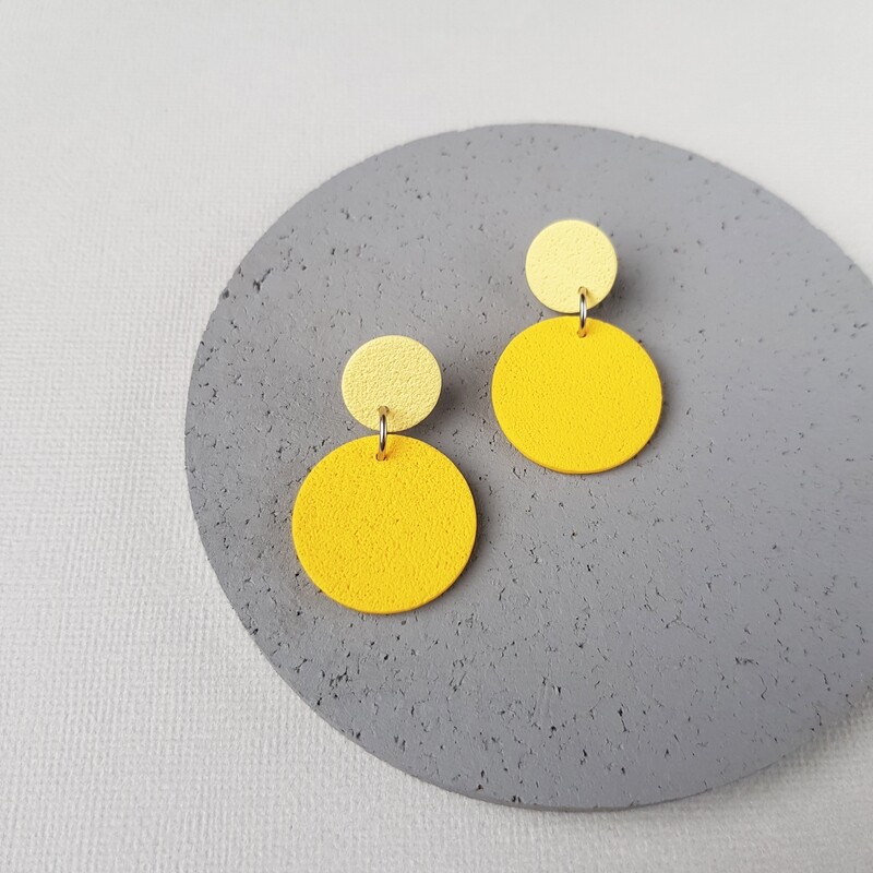 A pair of yellow and cream coloured circle earrings. The earrings are made of polymer clay and have a textured surface.