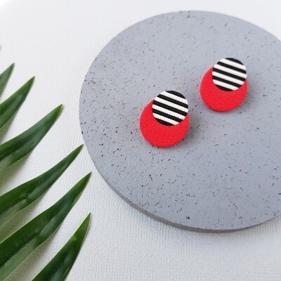 A circle pair of studs with a black and white striped pattern on the top half and a solid textured red colour on the bottom.