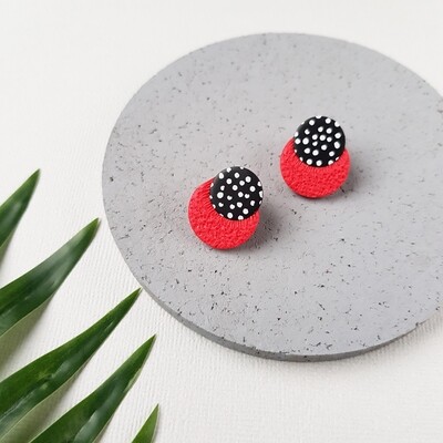 A pair of red studs with white polka dots on the upper black circle featuring a textured design. 