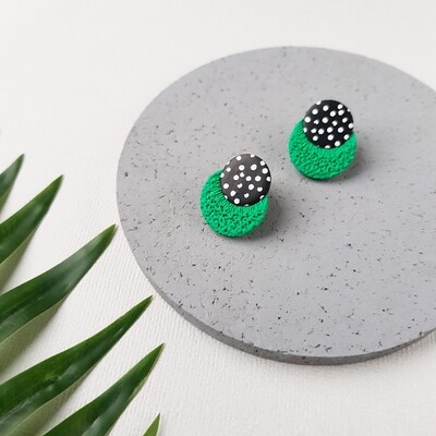 A pair of green, black and white polka dot earrings. The earrings are made of polymer clay and have a textured finish.