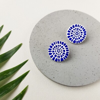 A pair of white polymer clay earrings with a blue mosaic pattern. The earrings are round and they're put on a grey background