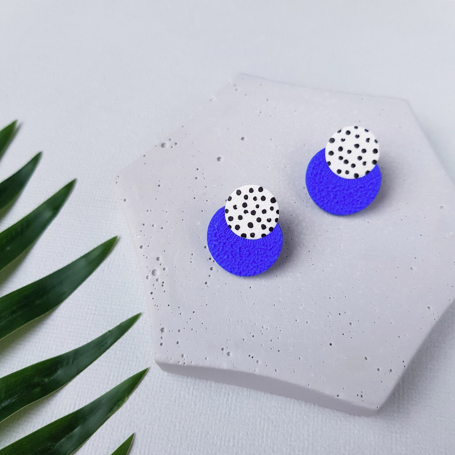 A pair of blue and white polka dot earrings. The earrings have two circles, one blue and one white, with black polka dots.