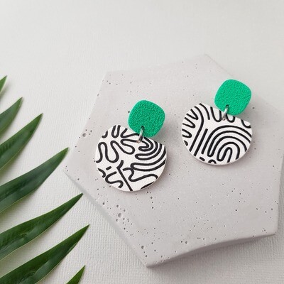 A pair of earrings with a white and black abstract pattern on a rounded base and a bright green square top bead.