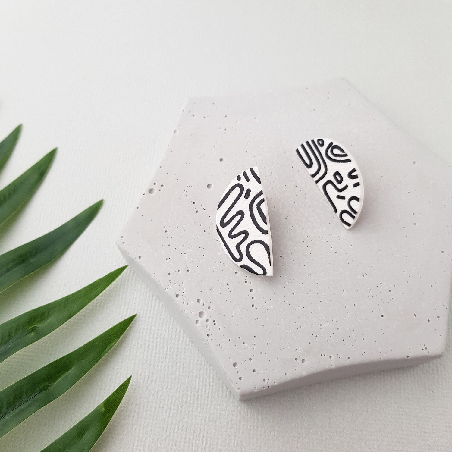 A pair of white polymer clay earrings with a black abstract pattern. The earrings are shaped like half-circles.