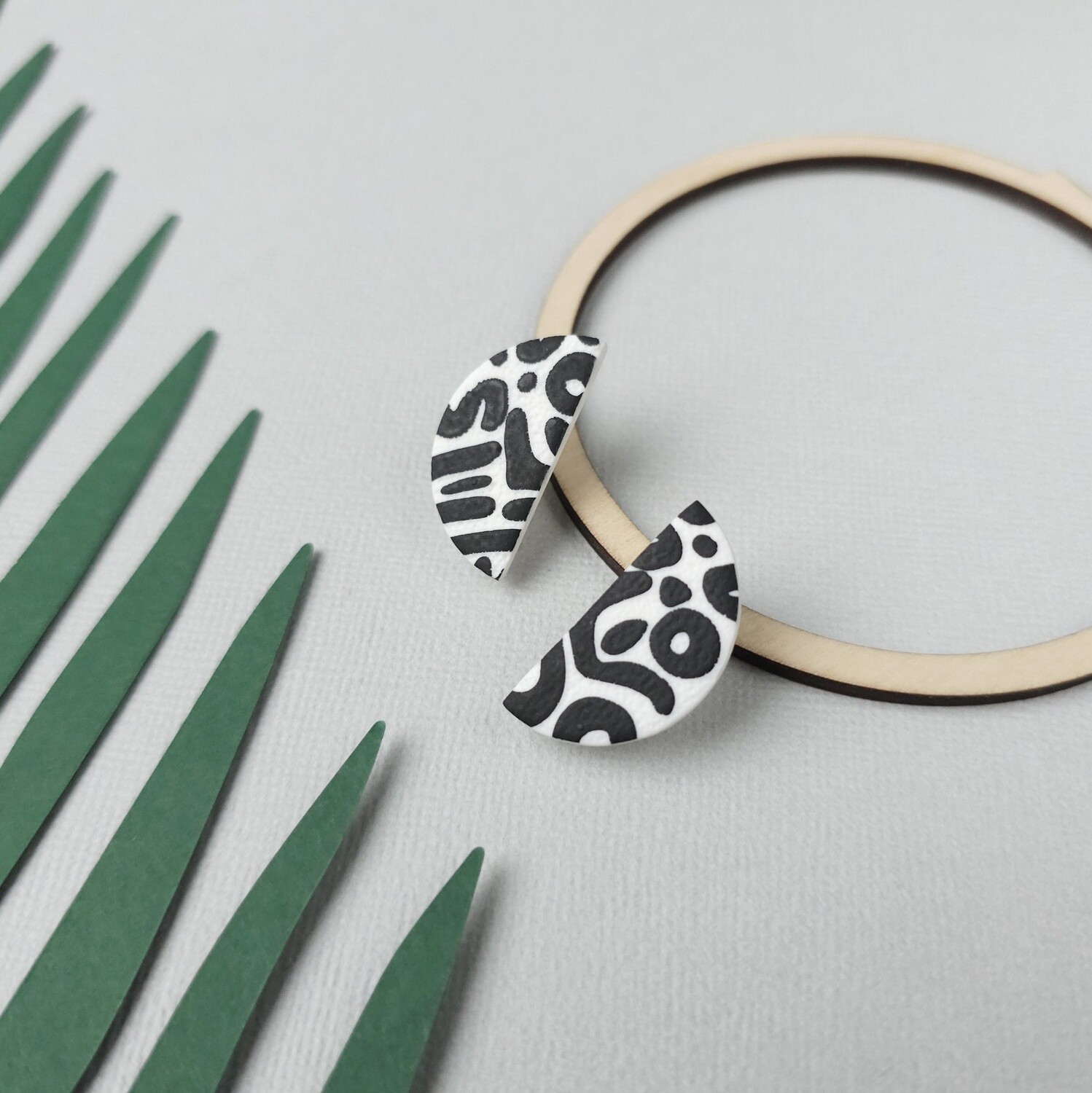 A pair of half-moon polymer clay earrings featuring a black and white abstract design.