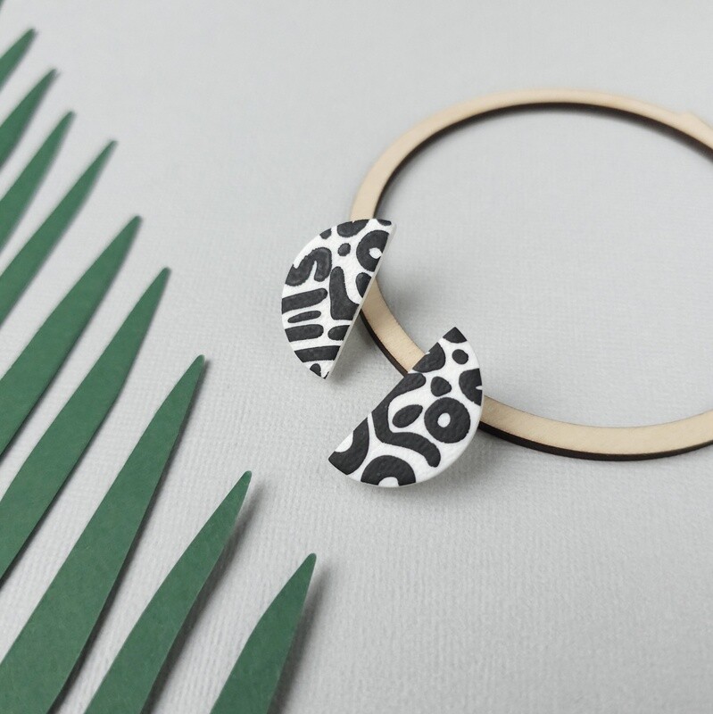 A pair of half-moon polymer clay earrings featuring a black and white abstract design.
