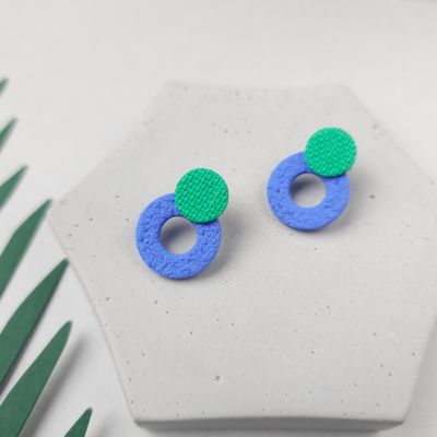 A pair of blue and green stud earrings, which feature a small green circle on top of a larger blue circle hoop at the bottom.