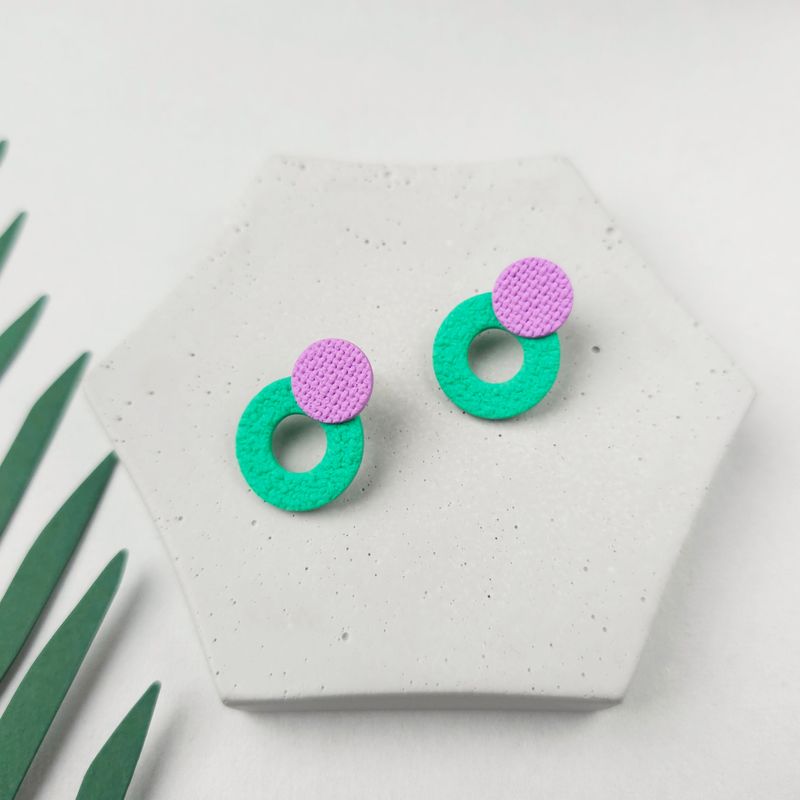 A pair of contemporary textured earrings with a lower bright green circle hoop and a smaller purple round top bead. 