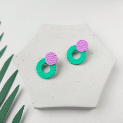A pair of contemporary textured earrings with a lower bright green circle hoop and a smaller purple round top bead. 