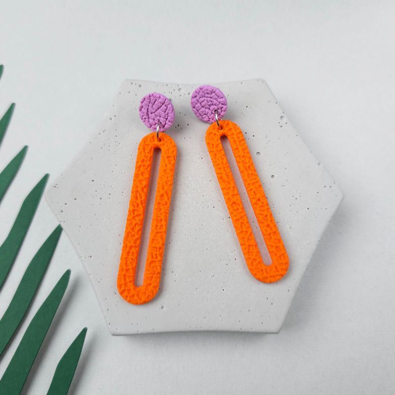 A pair of orange and purple dangle earrings with a textured finish that are shaped like a very long rectangle rounded hoop.