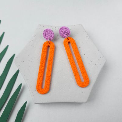 A pair of orange and purple dangle earrings with a textured finish that are shaped like a very long rectangle rounded hoop.