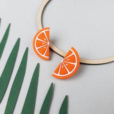 Bright orange slice earrings with white detailing and a textured surface.