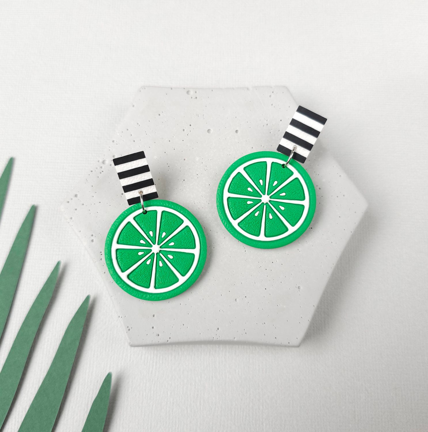 A pair of lime green earrings with black and white striped upper bead. Each earring features a lime slice design.