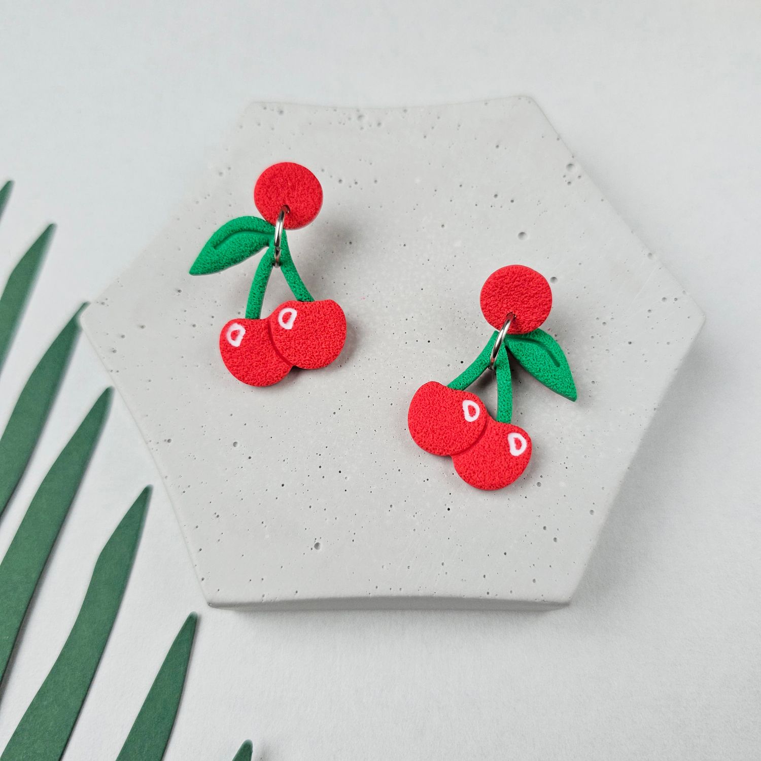 A small pair of red cherry earrings with green leaves.
