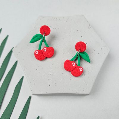 A small pair of red cherry earrings with green leaves.