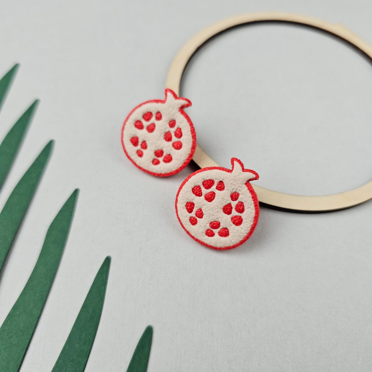Two polymer clay pomegranate studs, that are cream-coloured with red seeds and a red outline.