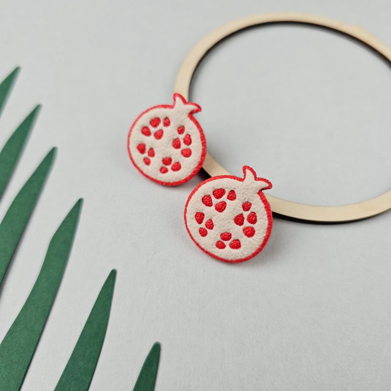 Two polymer clay pomegranate studs, that are cream-coloured with red seeds and a red outline.