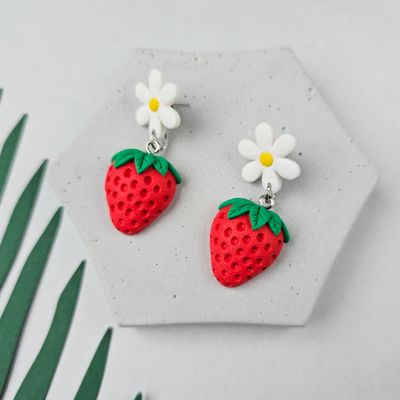 The earrings showcase a white daisy with a yellow centre and a red strawberry with green leaves