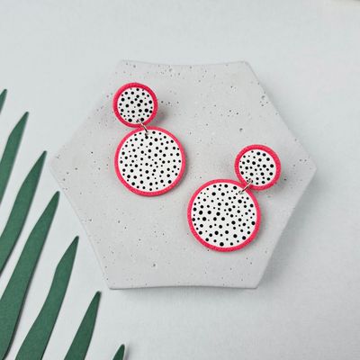 A pair of stud earrings with a white and black polka dot design. The earrings have a pink rim and are made of polymer clay.
