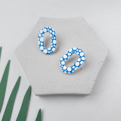 A pair of white and blue small oval hoops, made from polymer clay. They have a bubble pattern.