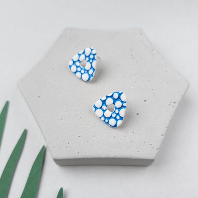 A pair of white and blue triangular stud earrings. The earrings have a pattern of white bubbles on a blue background.