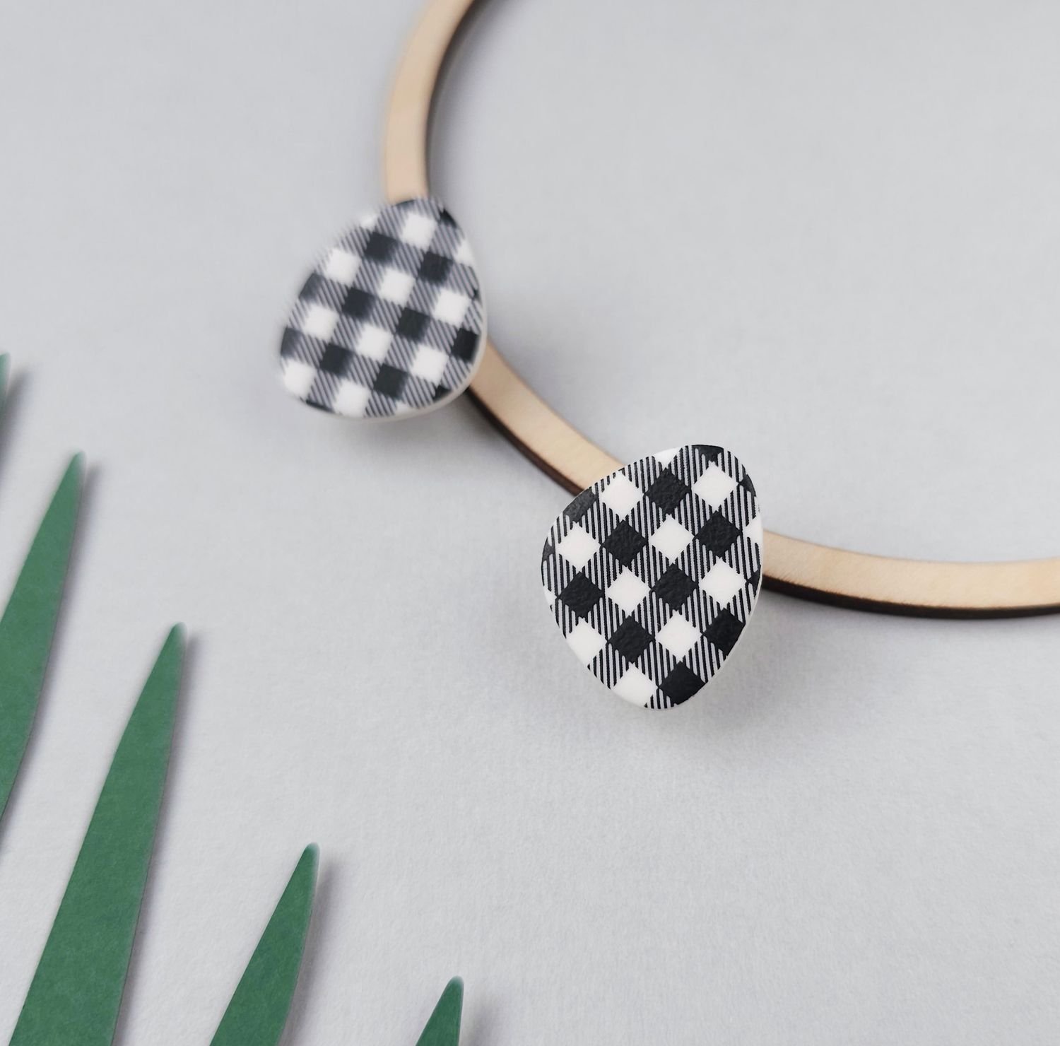 A pair of black and white gingham patterned earrings. The earrings are shaped like teardrops and made of polymer clay.